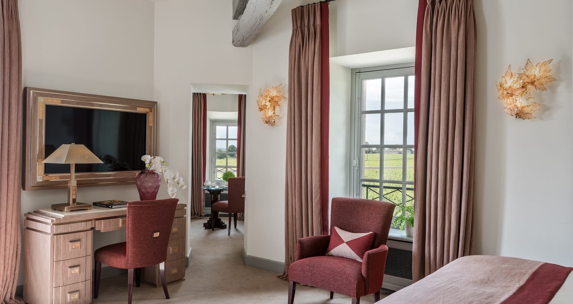 A suite at the château, French windows open to the vineyard, bedlinen pale against panelled walls.