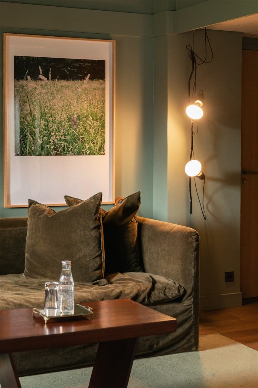 A junior suite with sage-green walls, an olive velvet sofa and a framed botanical photograph above.