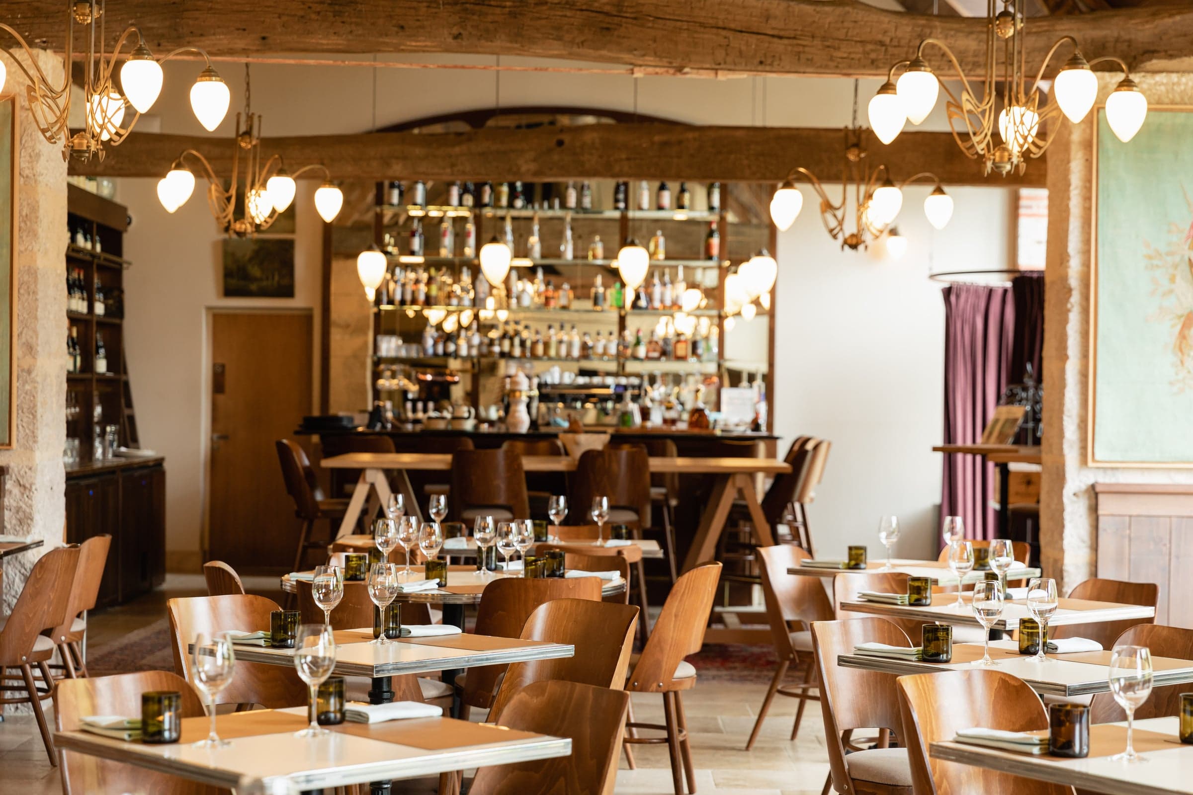 L'Auberge dining room, a long communal table set under timber beams and warm lamplight.