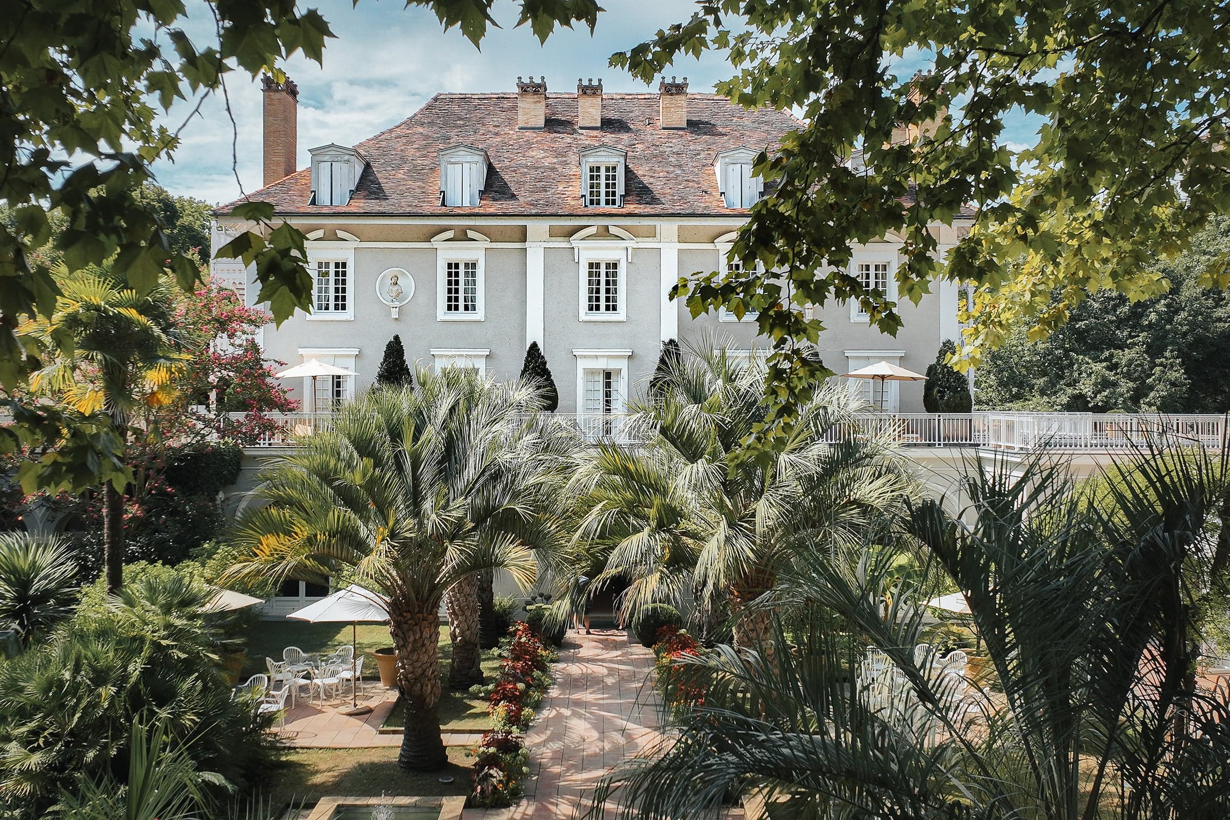 The main house at Les Prés d'Eugénie seen from the gardens, palms and parterres at midday.