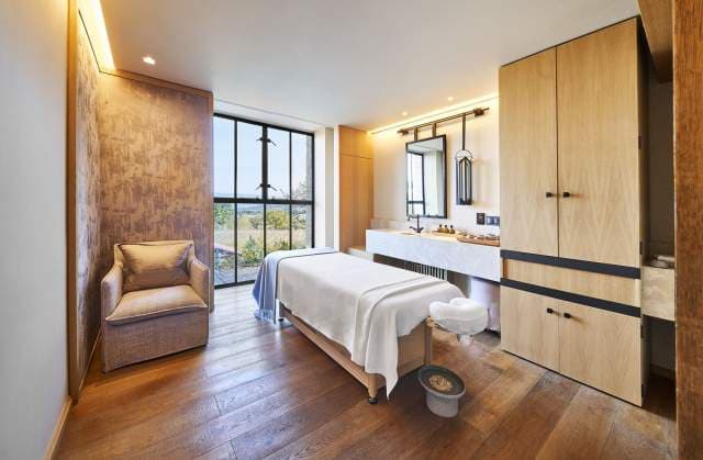 A spa treatment room with a wide window onto the estate, pale woods and a low daybed.