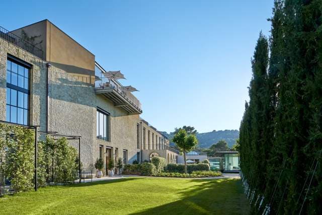 The Villa La Coste hotel building seen from the gardens, limestone façades and a tall cypress hedge against the Provence hills.
