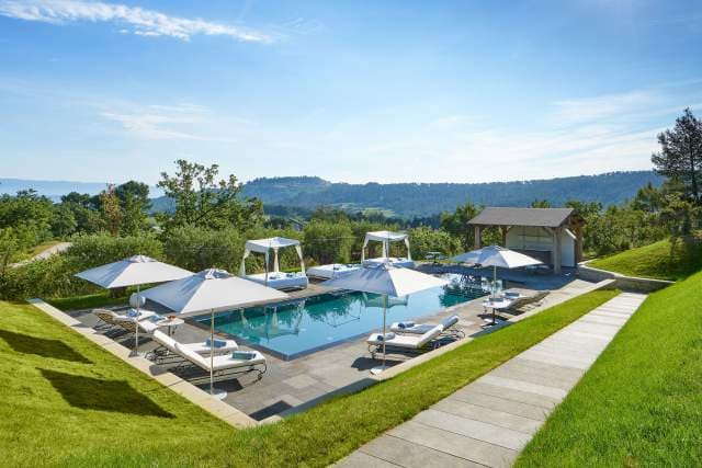 The Villa La Coste pool with parasols and lounge chairs, the Luberon valley falling away beyond.