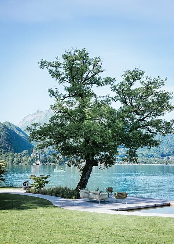 A lone tree on the auberge's lawn, two chairs and a sofa set on the deck at the water's edge.