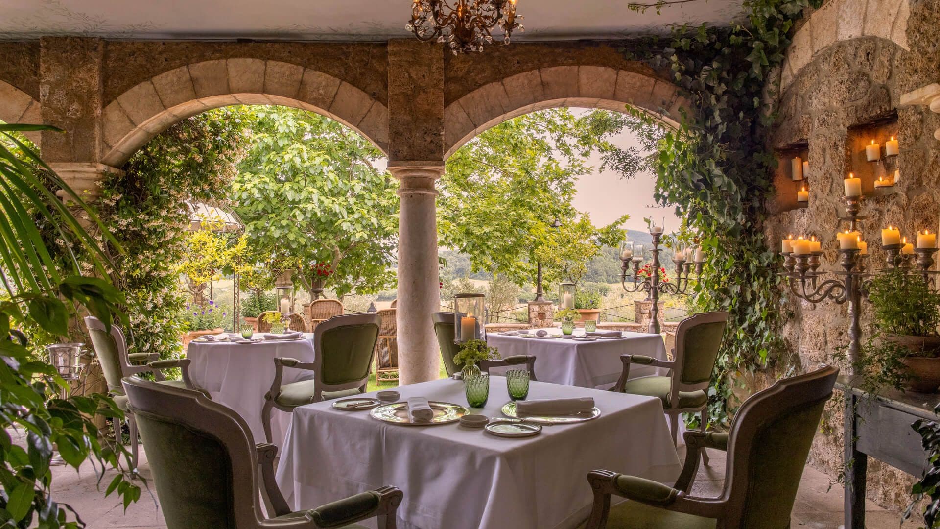 The Saporium dining loggia at Borgo Santo Pietro — stone arches over a single set table, the Tuscan landscape beyond.