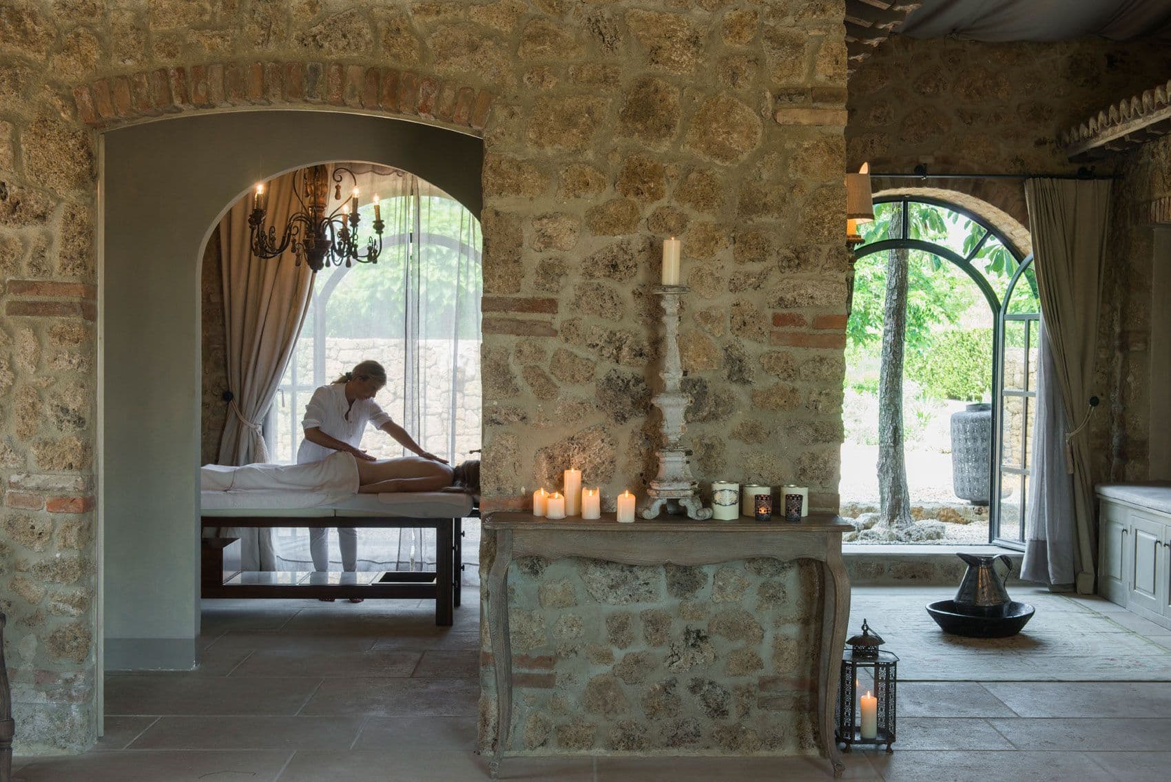 A Seed to Skin treatment room at Borgo Santo Pietro — stone walls, a stone candlestick, soft curtains framing an arched window.