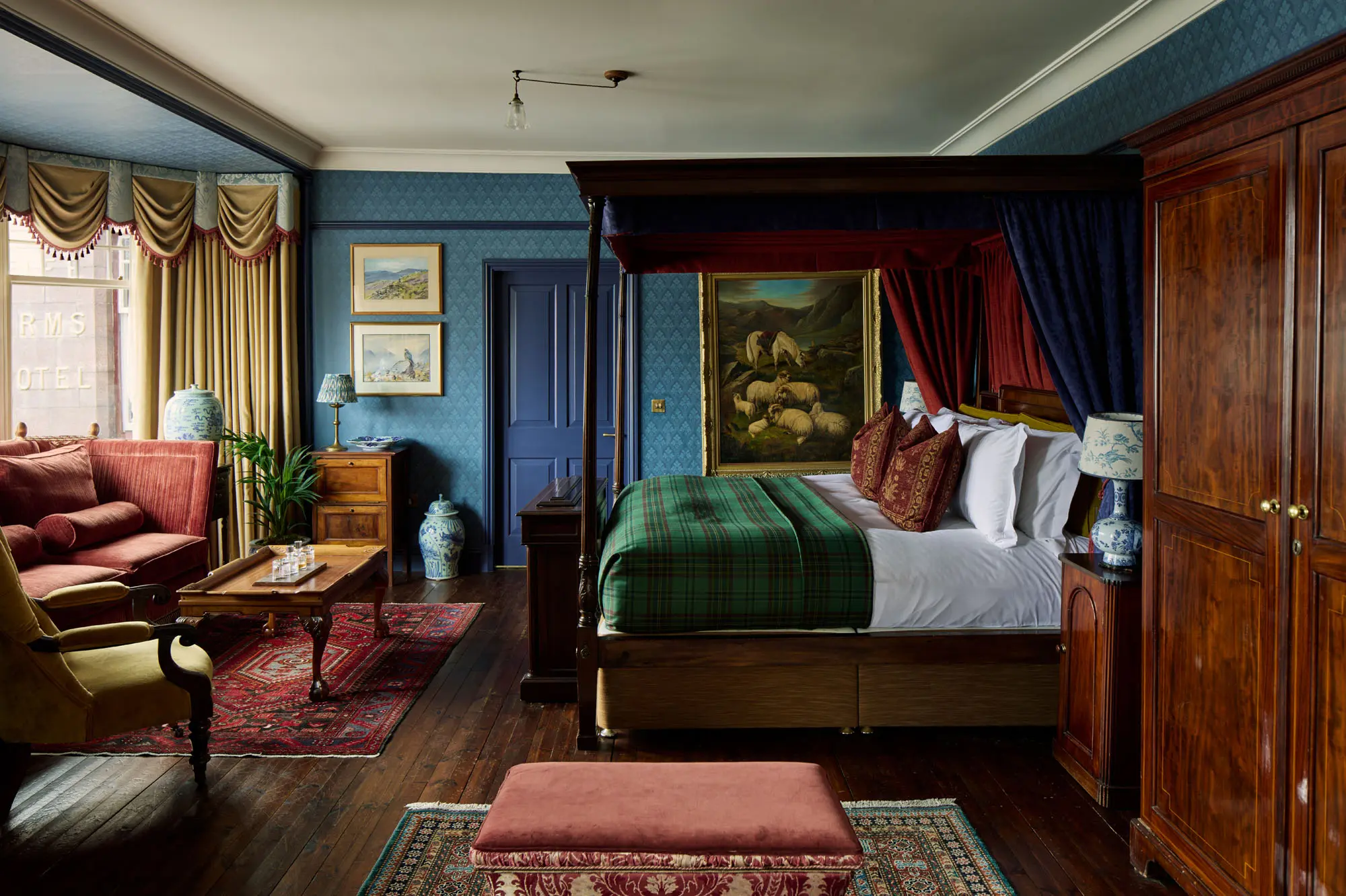 A four-poster bedroom in the Scottish style, deep blue walls, tartan blanket, a framed painting of sheep above the bed.