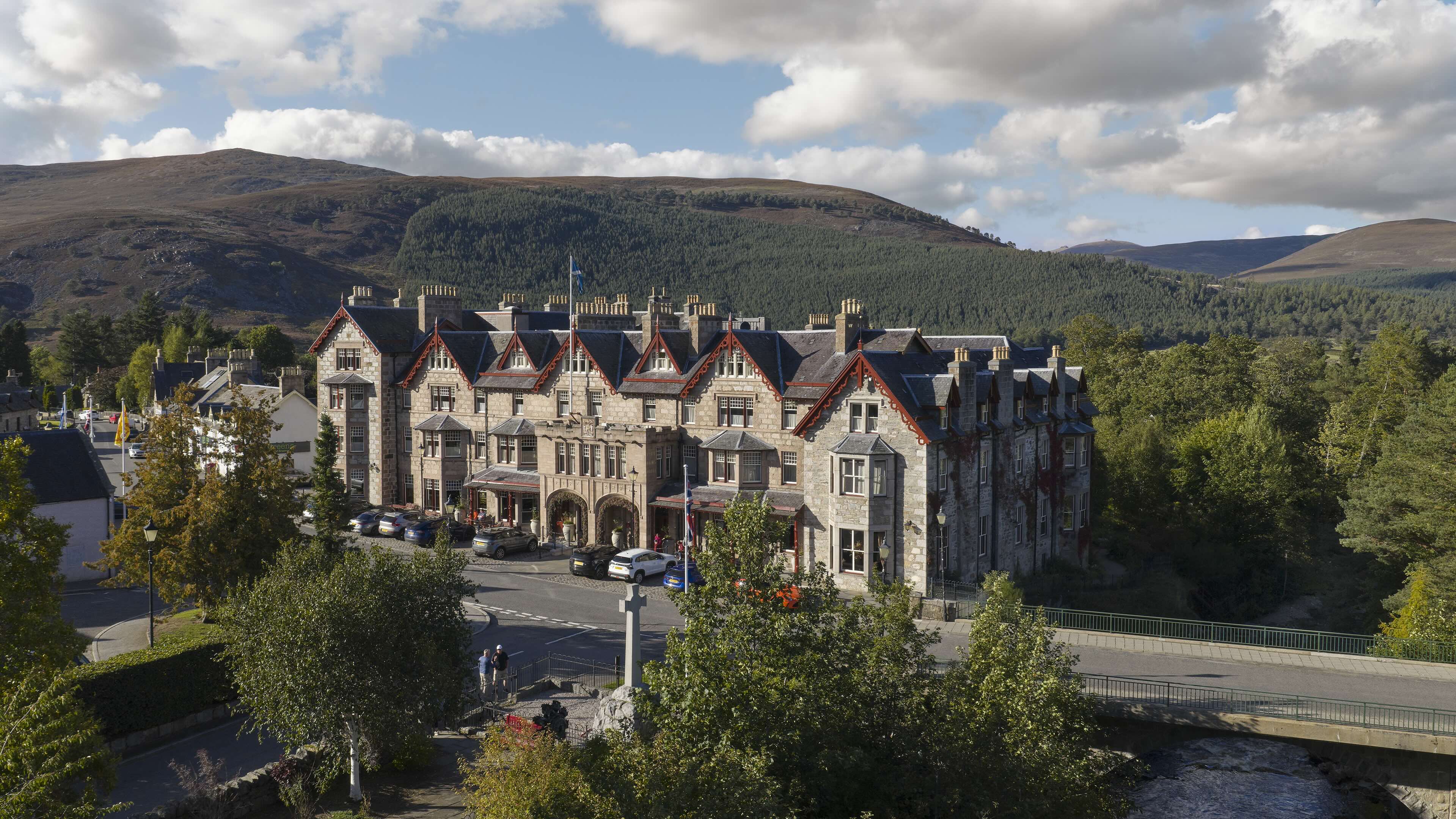 The Fife Arms seen from across the bridge in Braemar, the granite façade beneath low Highland cloud and the Cairngorm hills behind.