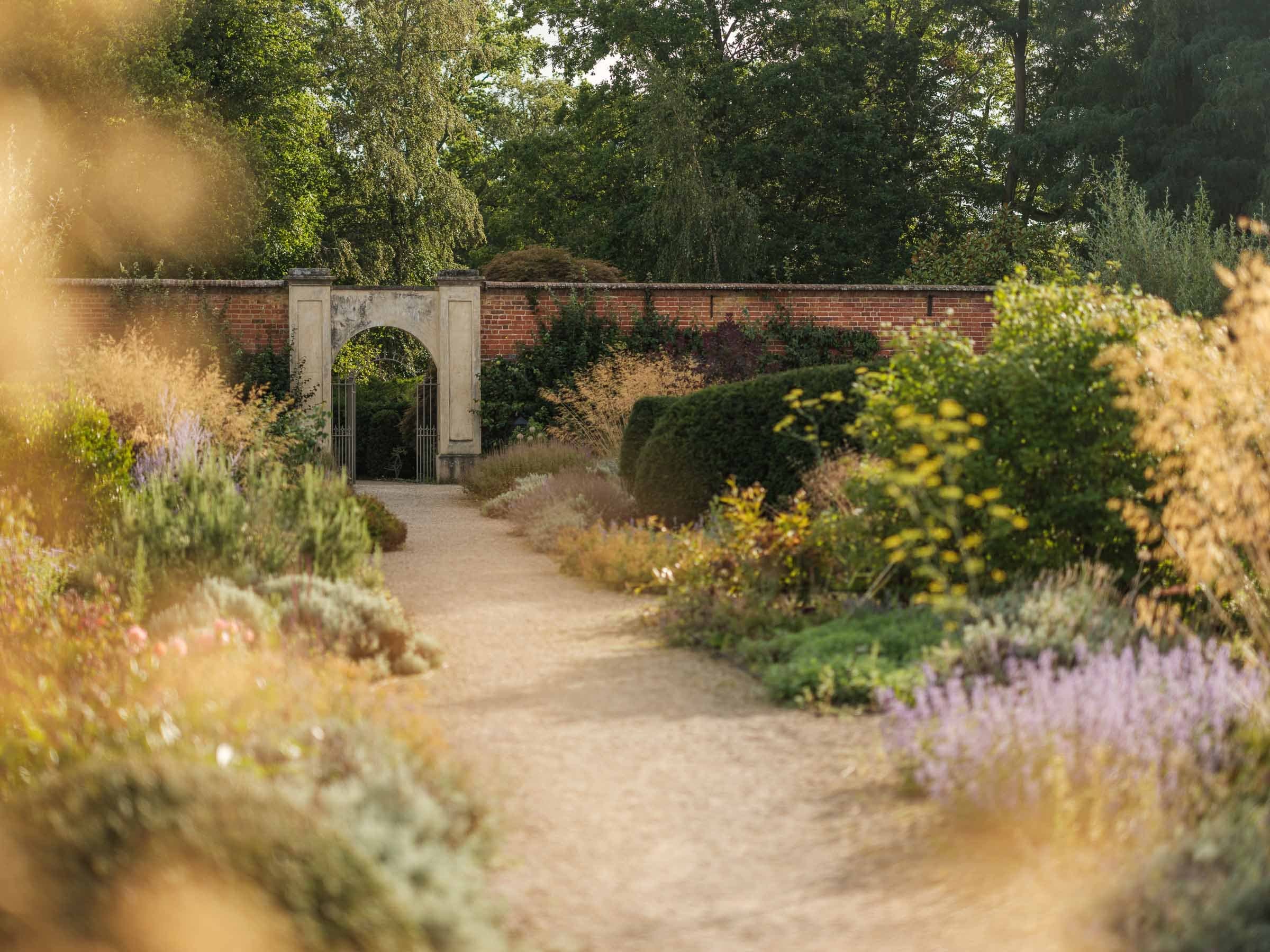 A view down the brick-walled kitchen garden, herbs and salads laid out in long beds beneath a high wall.