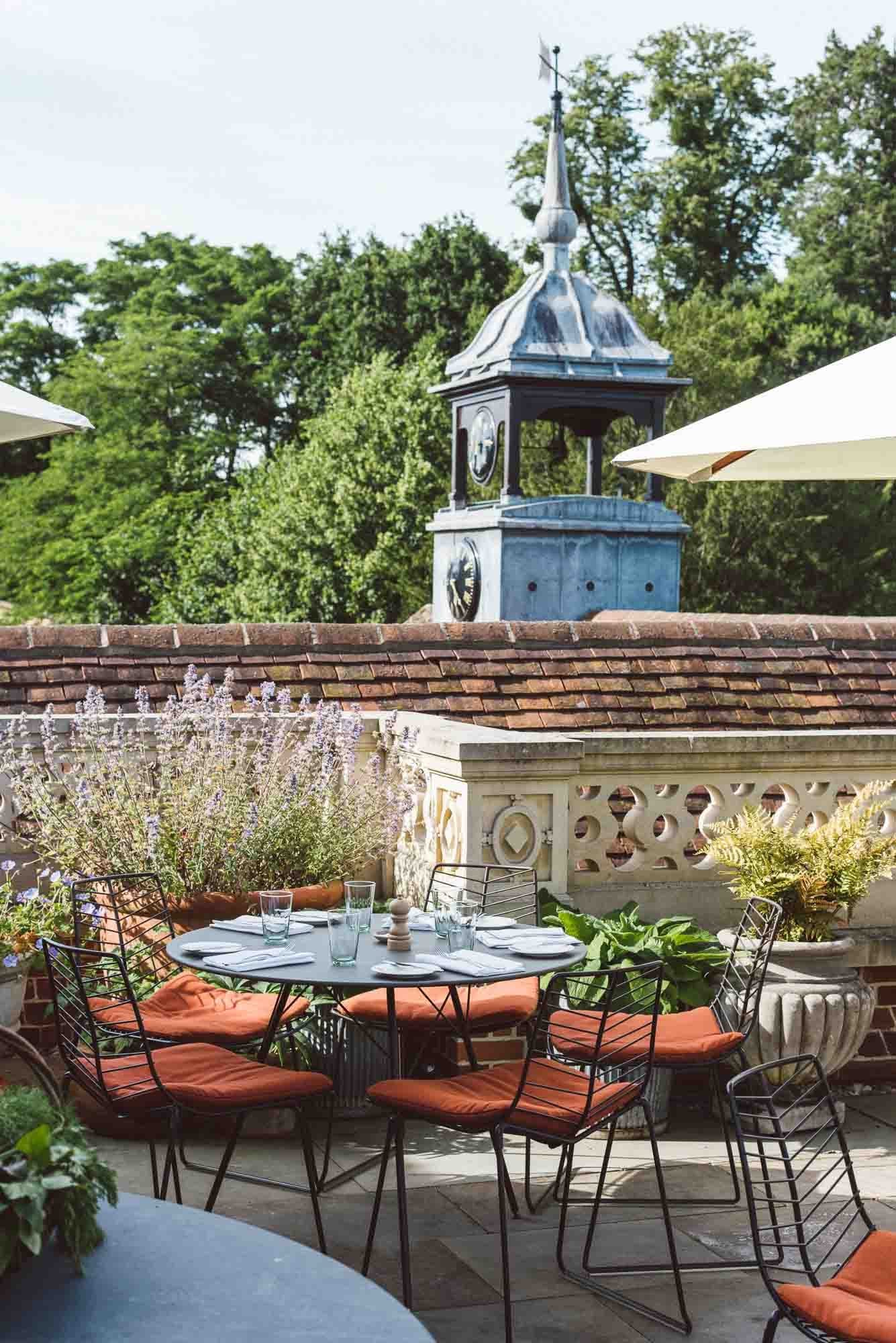 A pale terrace table at Marle laid with linen and glassware, the gardens visible just beyond.