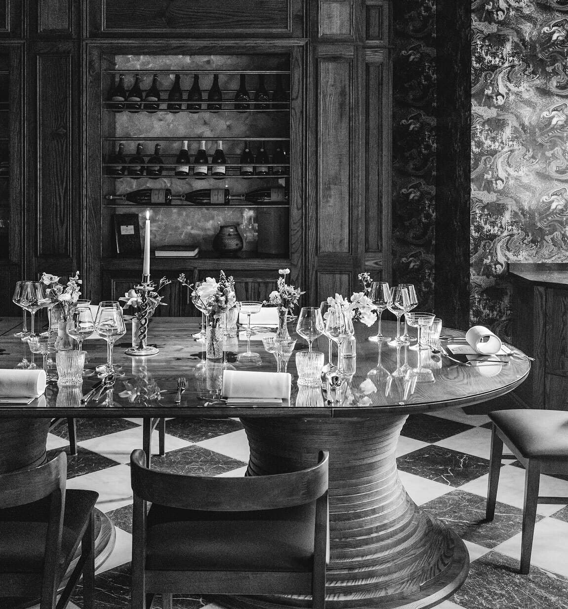 The Hearth chef's table — a long oak table dressed for dinner, a marbled checkerboard floor underfoot.
