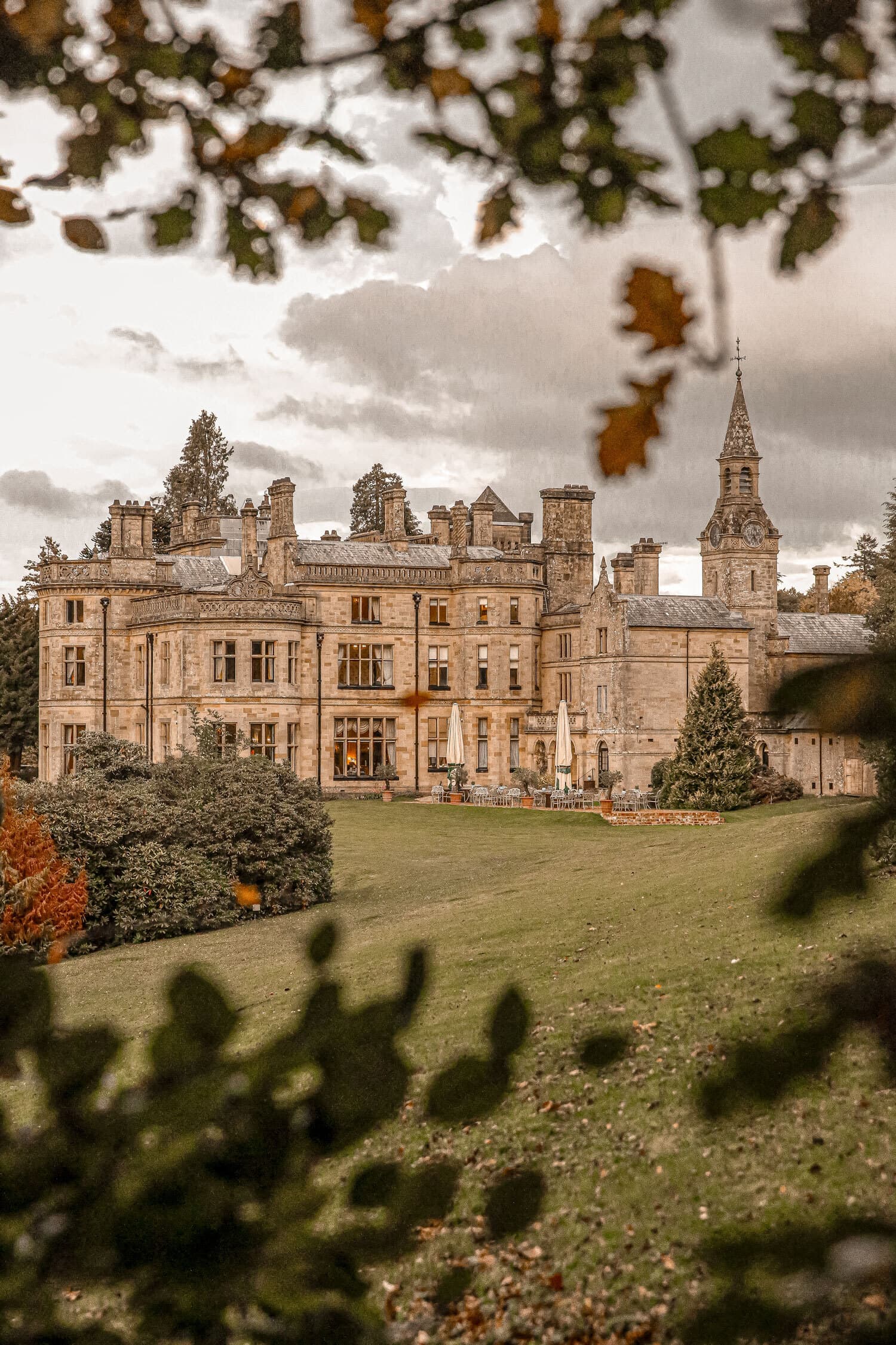 The Victorian façade of Palé Hall seen from the gardens, autumn leaves framing the view, a tall clock tower at the right.