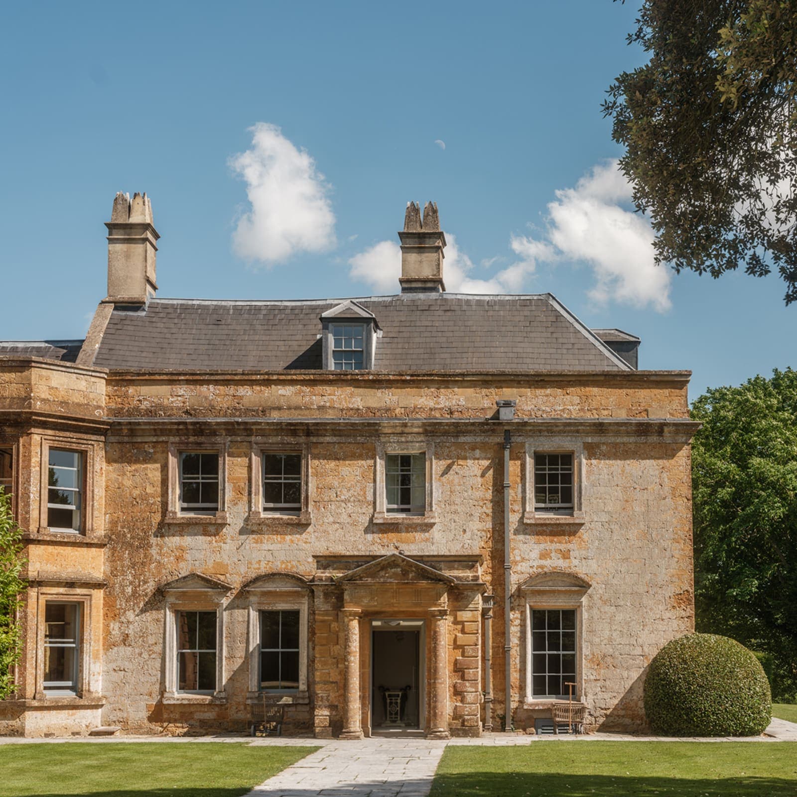 The honey-stone Georgian facade of Hadspen House on a clear summer afternoon, lawns running up to the front door.