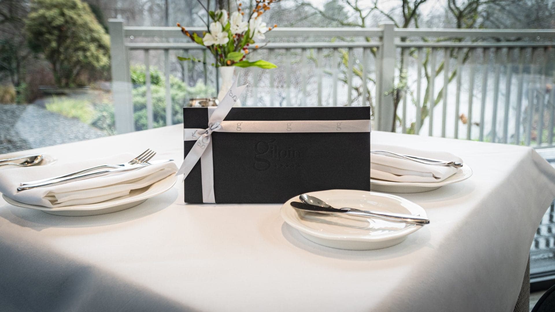 A table set on a glass-railed terrace overlooking winter woodland, white linen, fresh flowers and the kitchen's leather-bound menu.